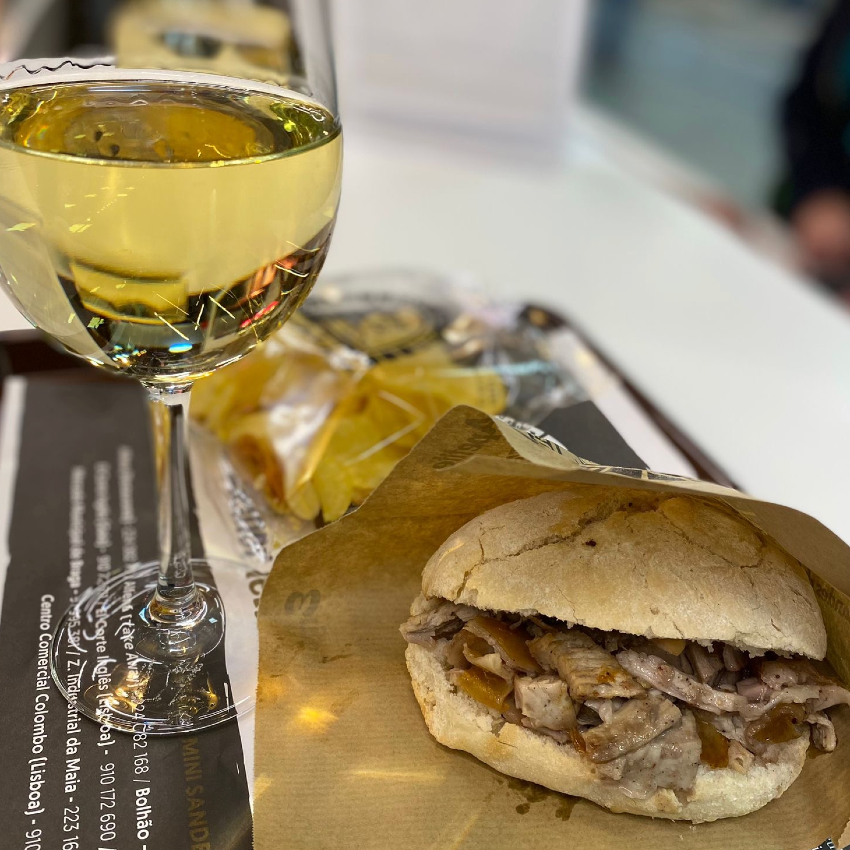 A fresh round bun filled with roasted pork, served with a large glass of white wine